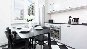 Ett modernt kök med vita skåp, en svart bänkskiva och en matplats med ett svart bord och stolar.