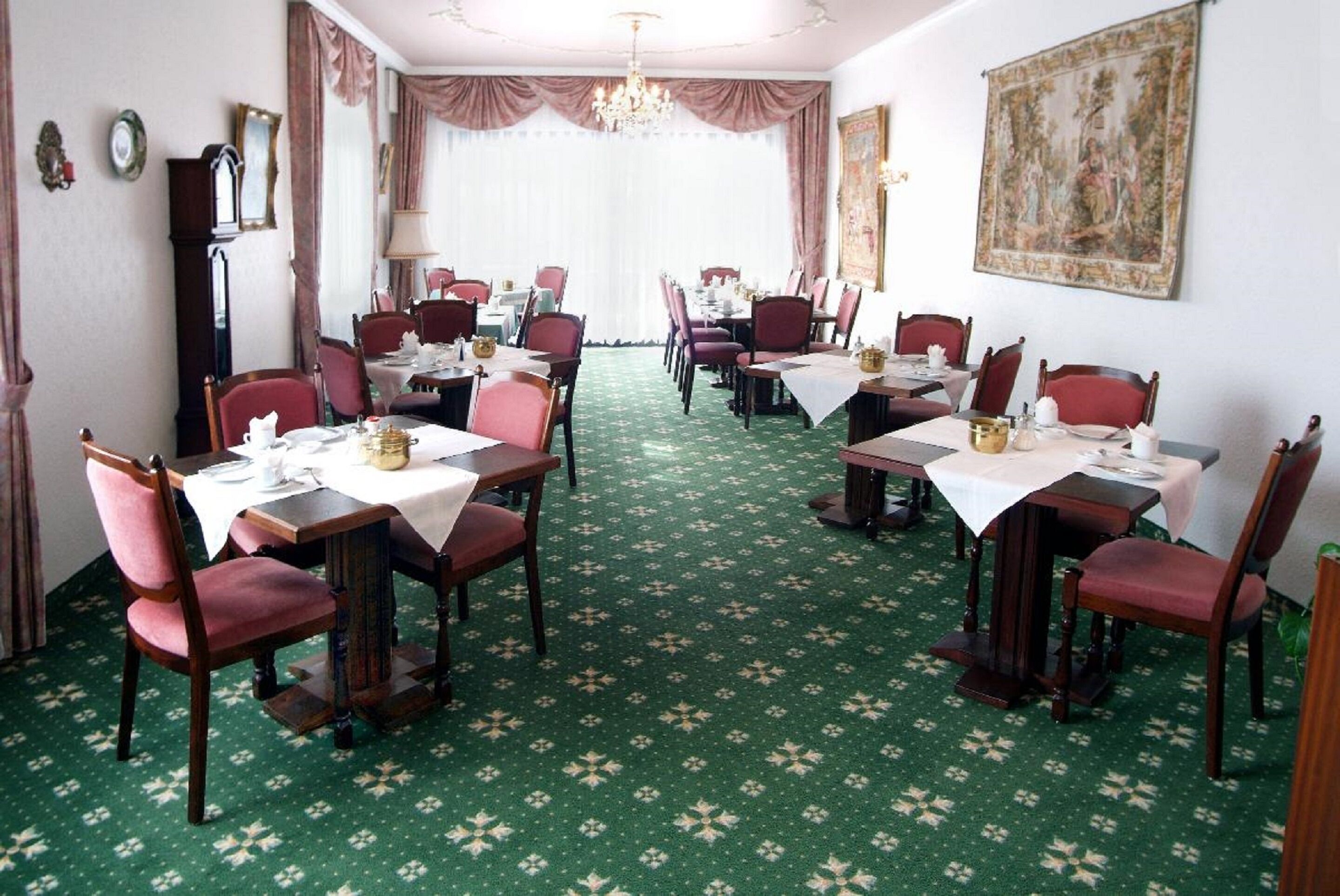 A dining area with multiple tables and chairs, a chandelier, and a large painting on the wall.