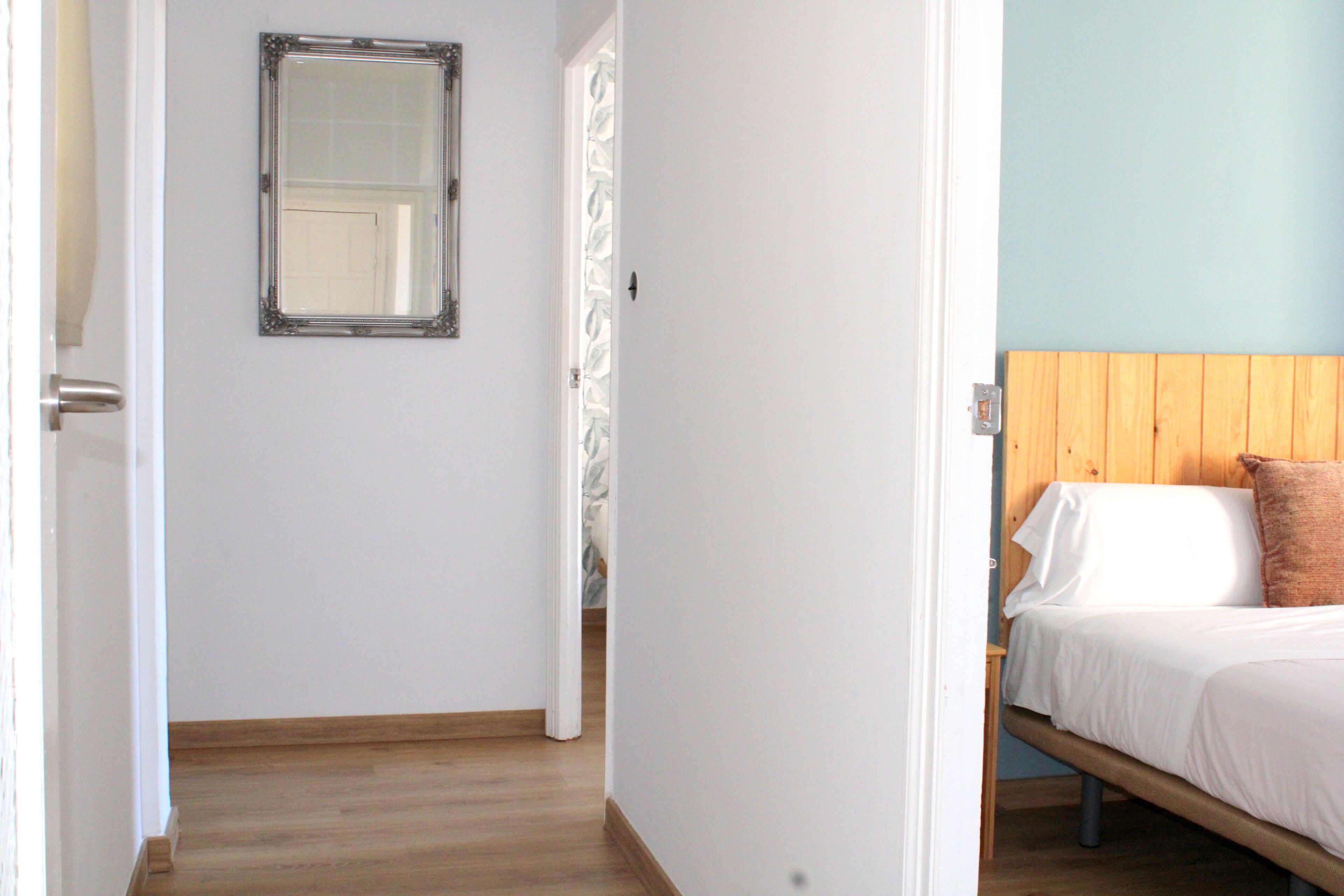 A bedroom with a wooden headboard, a bed with white bedding, and a mirror on the wall.