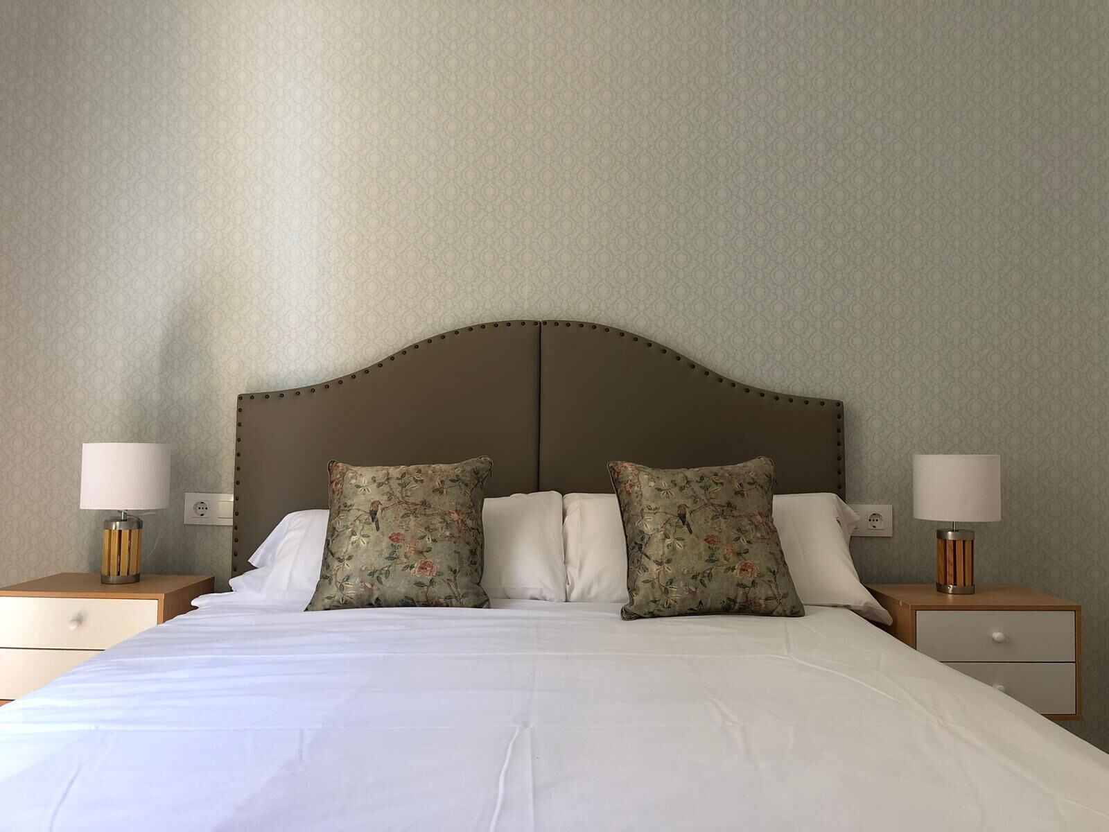 A bed with two floral pillows, a wooden headboard, and two bedside tables with lamps.