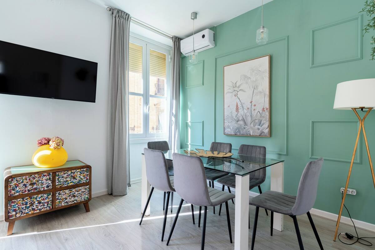 A dining area with a glass table, grey chairs, a yellow vase, and a patterned sideboard.