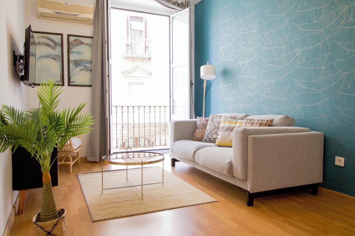A living room with a sofa, a coffee table, a potted plant, and a view of the outside balcony.