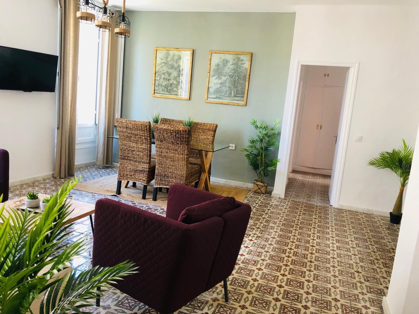 Uma sala de estar com sofá, duas cadeiras de vime, uma mesa de jantar e duas imagens emolduradas na parede.