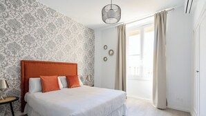 Un dormitorio con una cama, una mesita de noche, una lámpara, una ventana con cortinas y un papel tapiz estampado en la pared.