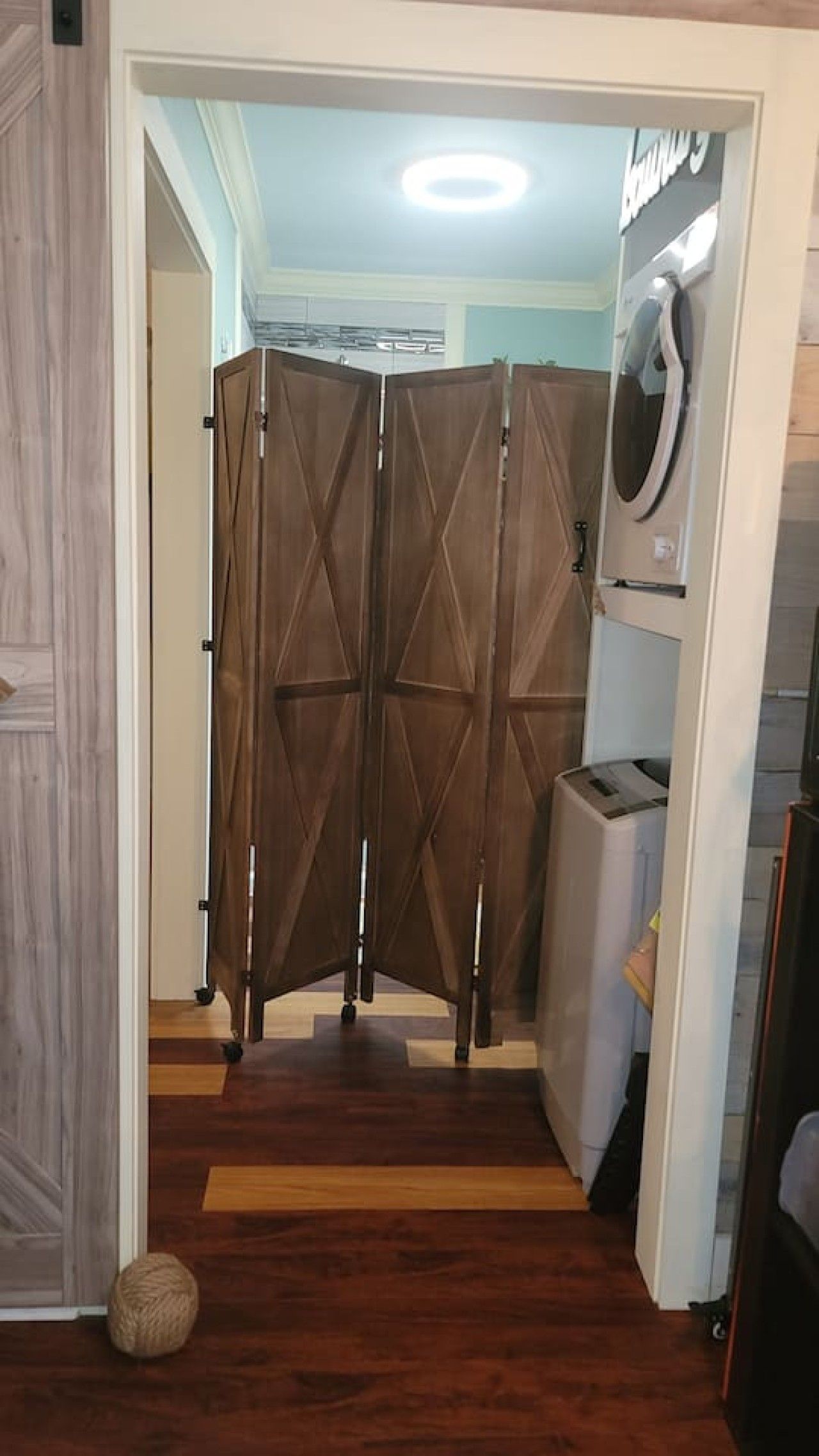 Una stanza con pavimento in legno, una porta bianca e una lavatrice fissata al muro.