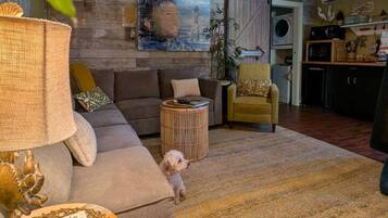Un soggiorno con un divano, un tavolino rotondo con un oggetto decorativo, un cane e una parete con un quadro.
