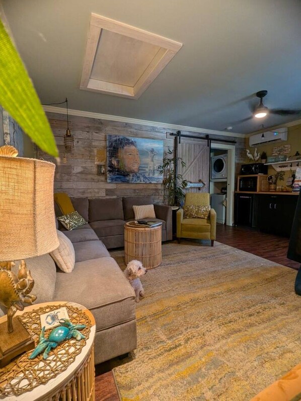 A living room with a sofa, a small round table with a decorative item, a dog, and a wall with a painting.