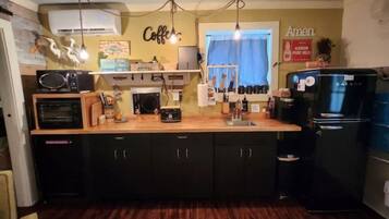Une cuisine compacte avec un plan de travail en bois, des placards noirs, un four encastré, un réfrigérateur et un panneau décoratif représentant une tasse de café accroché au mur.