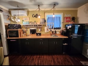 A compact kitchen with a wooden countertop, black cabinets, a built-in oven, a refrigerator, and a coffee sign on the wall.