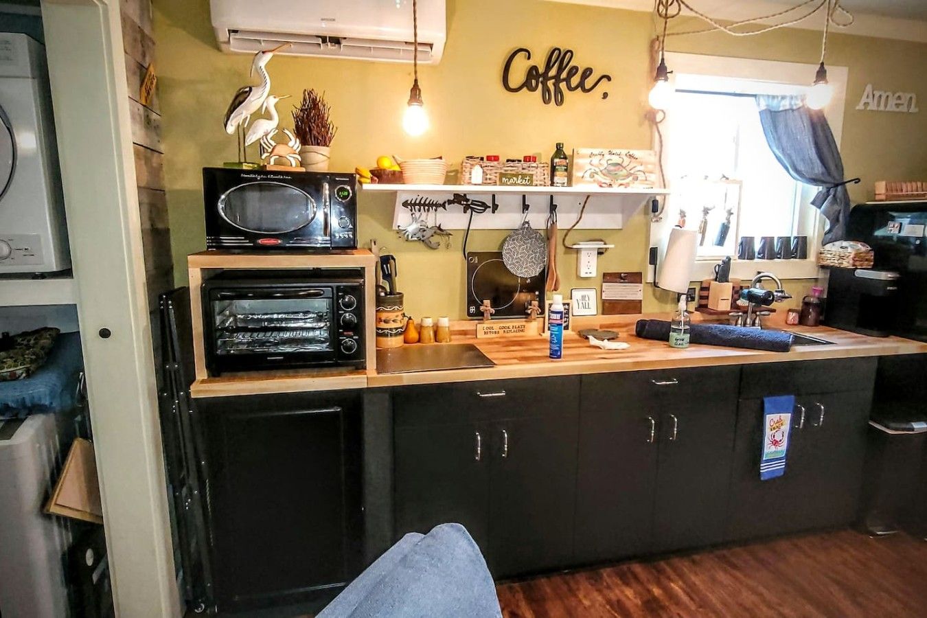 A compact kitchen with a microwave, toaster, and a coffee-themed wall sign.