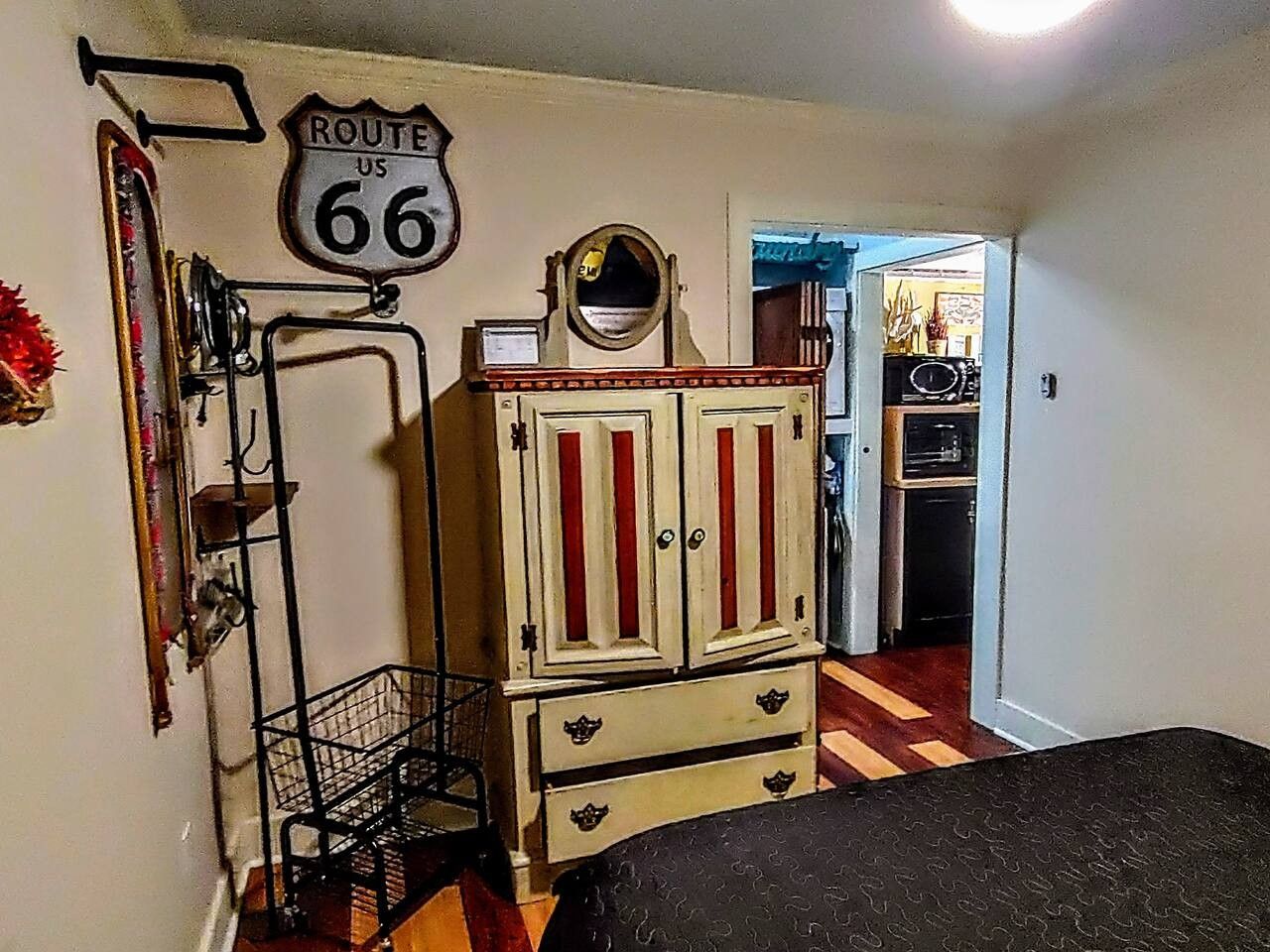Una stanza con un letto, un armadio, uno specchio, una mensola con oggetti decorativi e una porta che dà su un'altra stanza.