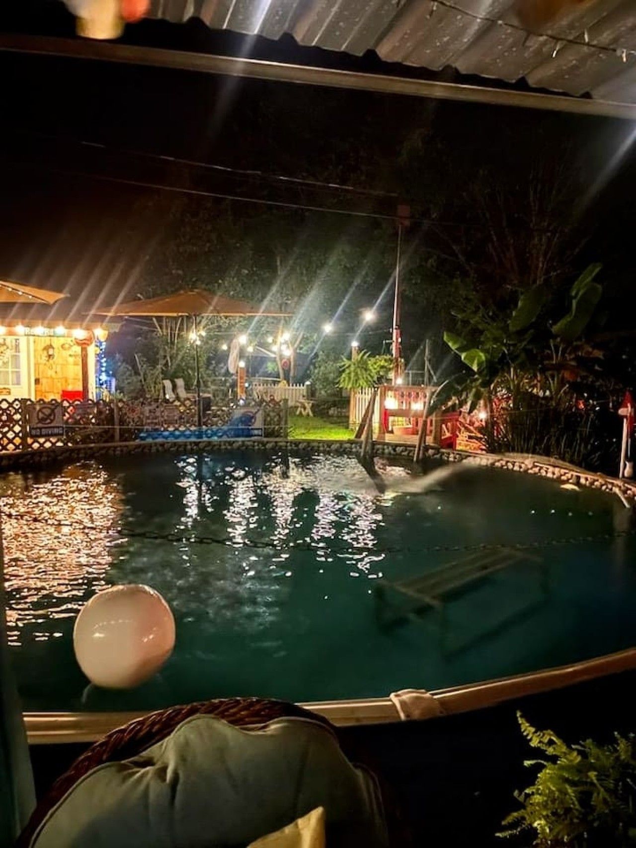Vista notturna di un'area piscina con uno scivolo acquatico, lettini e un piccolo edificio illuminato.