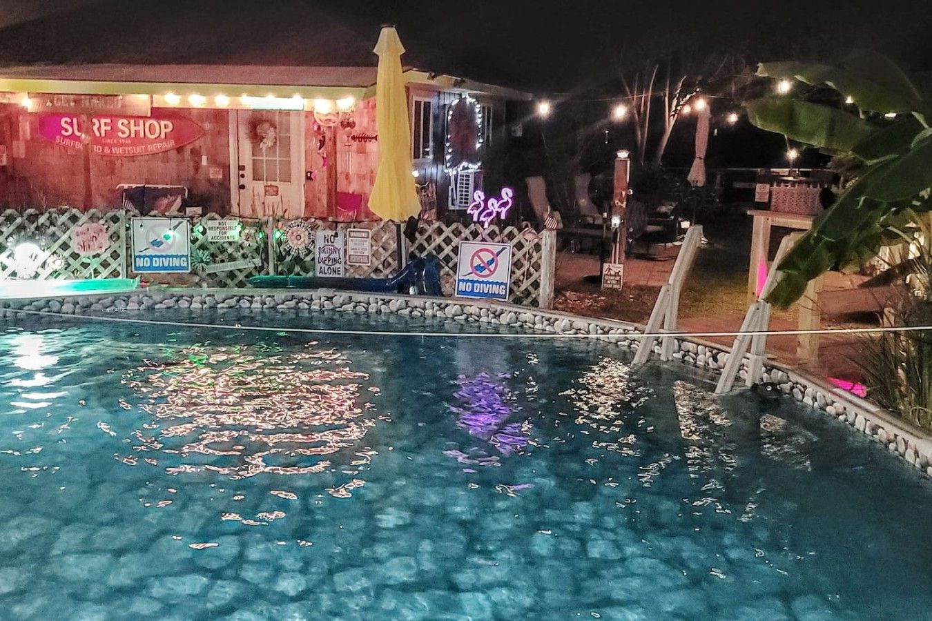 A swimming pool with a 'NO DIVING' sign, a surf shop, and decorative lights.