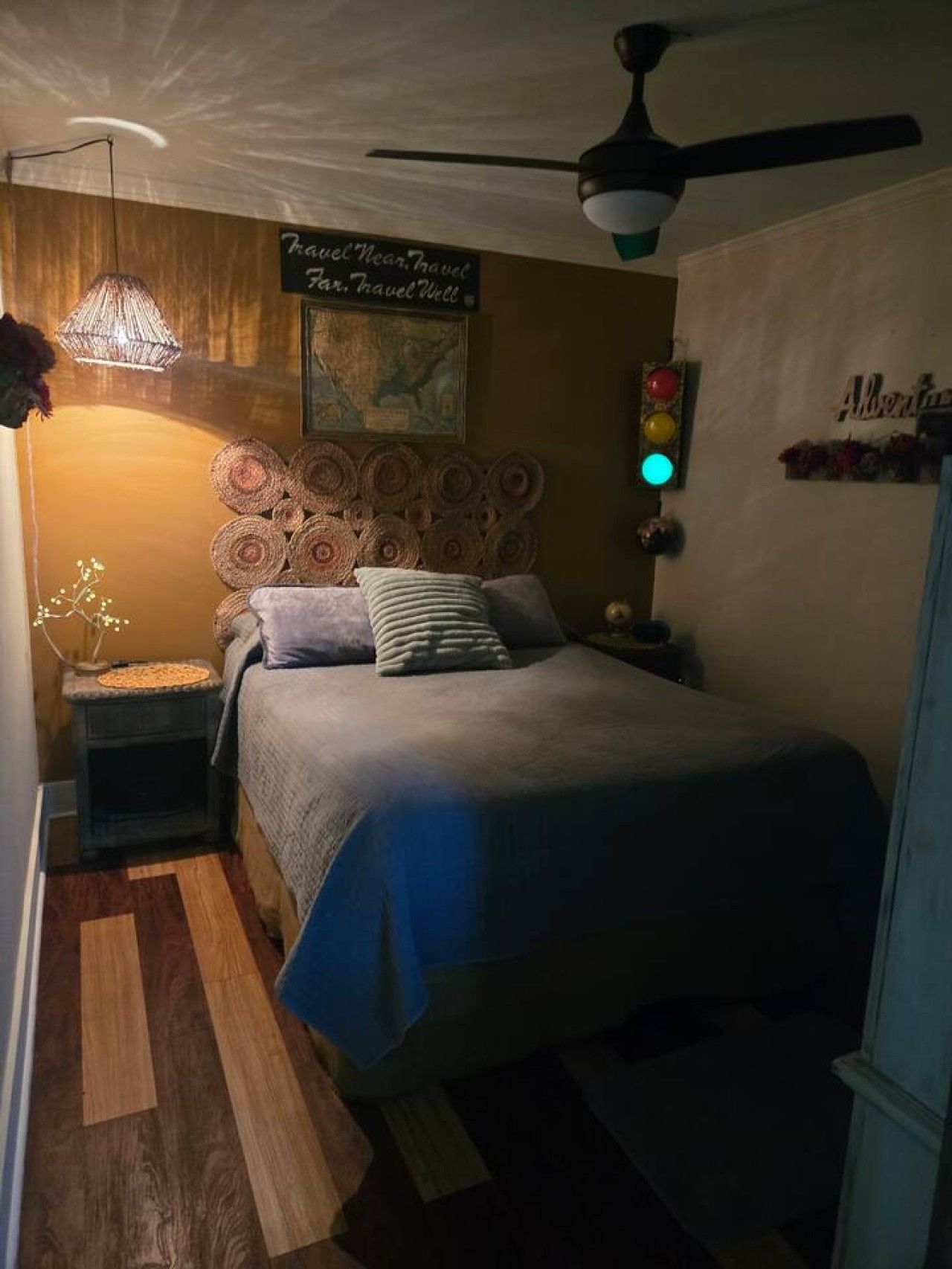 Une chambre à coucher avec un lit, une tête de lit ornée de motifs circulaires, un luminaire suspendu, une horloge murale et un ventilateur de plafond.