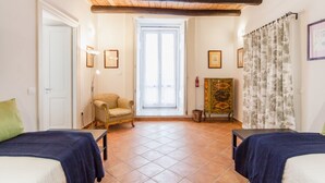 A room with two beds, a wooden ceiling, a door, a chair, a painting, and a window. - Palazzo Marigliano - Don Aniello (Napoli)