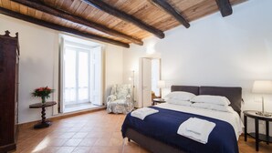 A bedroom with a large bed, a chair, a table, and a door leading to a balcony. - Palazzo Marigliano - Don Aniello (Napoli)