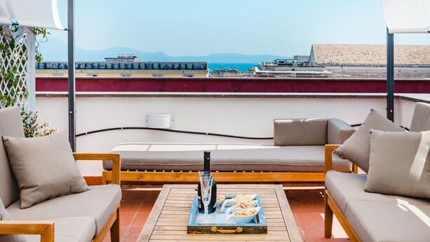 A rooftop terrace with a view of the sea, featuring a sofa set, a tray with snacks and a bottle, and a wooden table. - Don Francesco: an apartment with spectacular views in Palazzo Marigliano (Napoli)