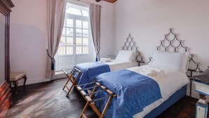 Une chambre avec deux lits, un plancher en bois, une fenêtre avec des rideaux et un plafond en bois.