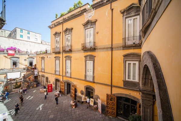 A courtyard with a yellow building, stone steps, and a few people.