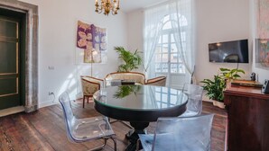 Un espace de salle à manger moderne avec une table et des chaises en verre, un lustre et une grande fenêtre agrémentée de rideaux légers.