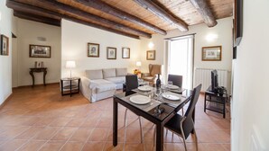 A dining area with a wooden table set for two, a sofa, and a small side table with a lamp.