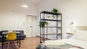 Una habitación moderna y luminosa con una cama, un escritorio con una silla, una estantería con plantas y una puerta.