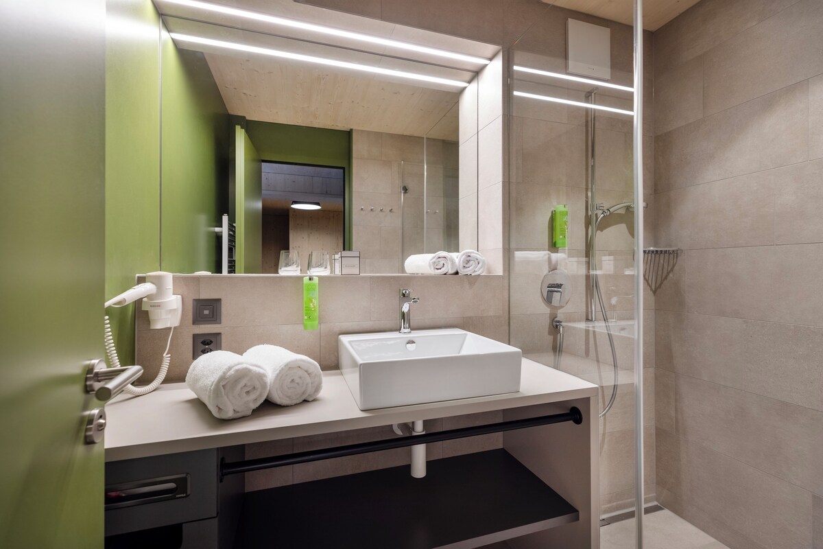 A modern bathroom with a white sink, green walls, and a glass shower enclosure.