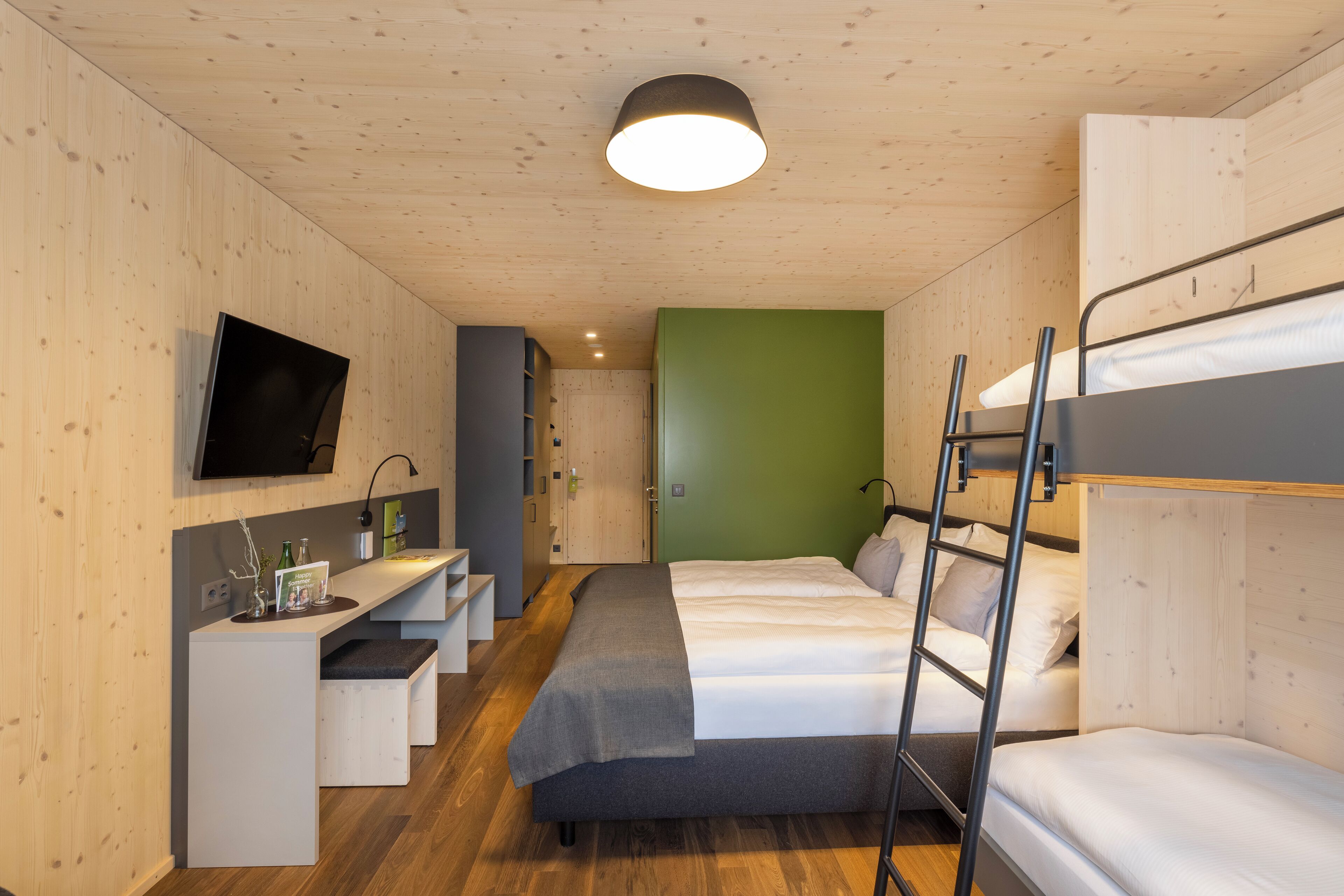 Ein Zimmer mit Etagenbetten, einem Schreibtisch und einem Flachbildfernseher sowie einer Wand in Grünton.