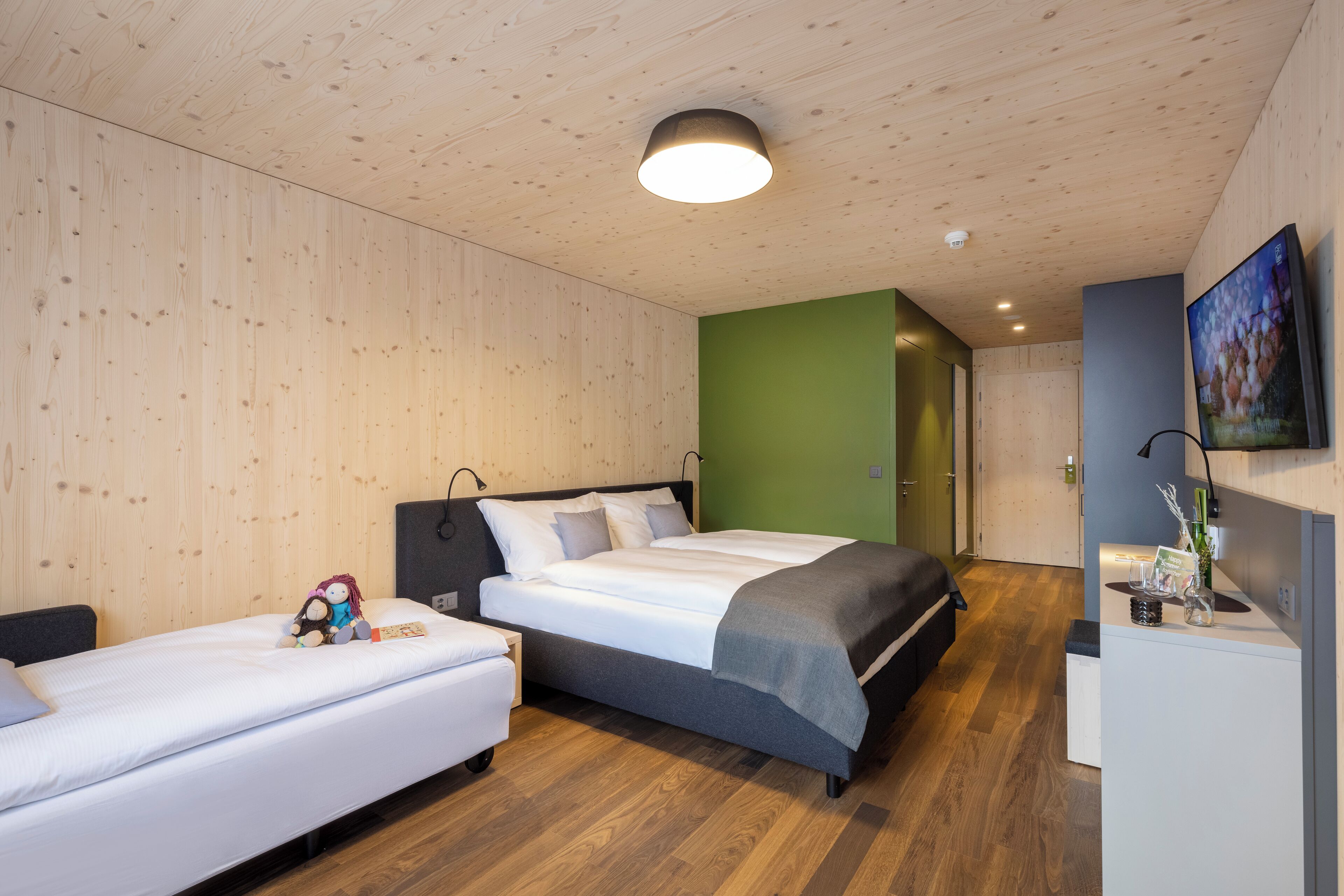 Ein modernes Schlafzimmer mit einem großen Bett, einem kleineren Bett und einem Schreibtisch mit Fernseher.