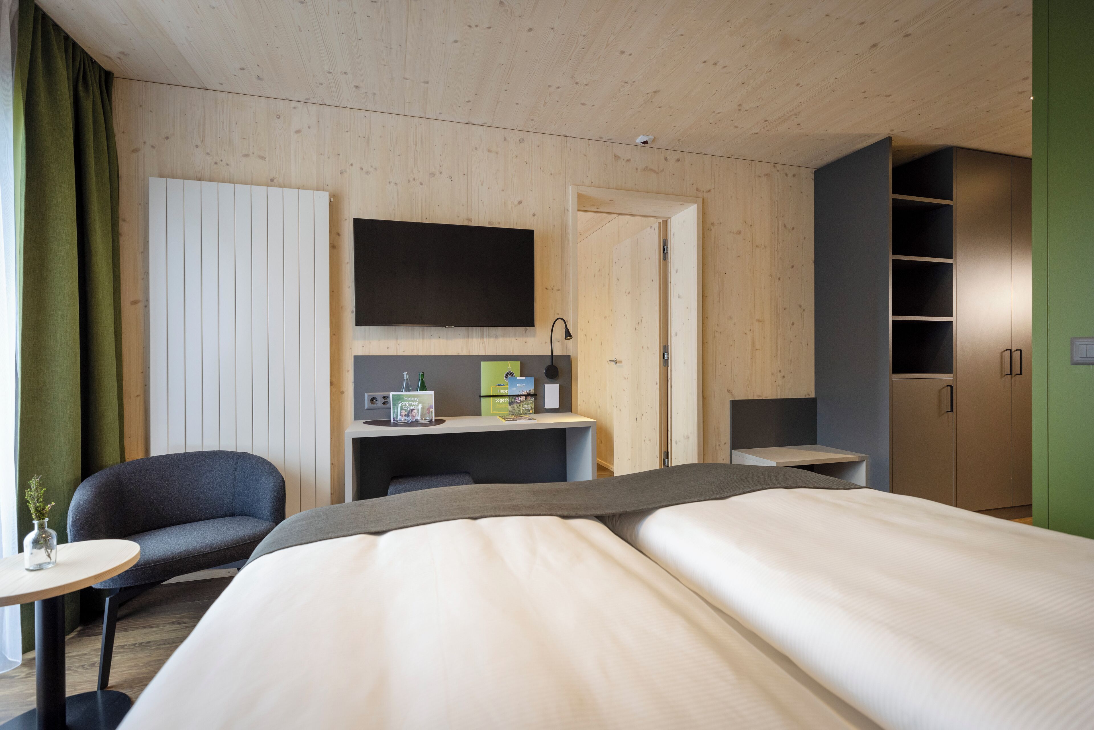 Een moderne hotelkamer met een houten plafond, een groot bed, een bureau met stoel, een aan de muur bevestigde televisie en een kledingkast.