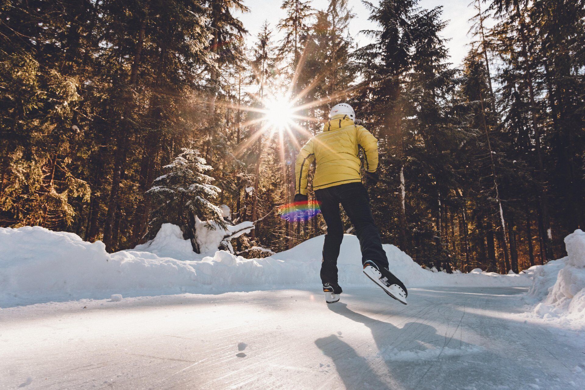A person ice skating on a frozen lake surrounded by snow-covered trees and a clear sky.