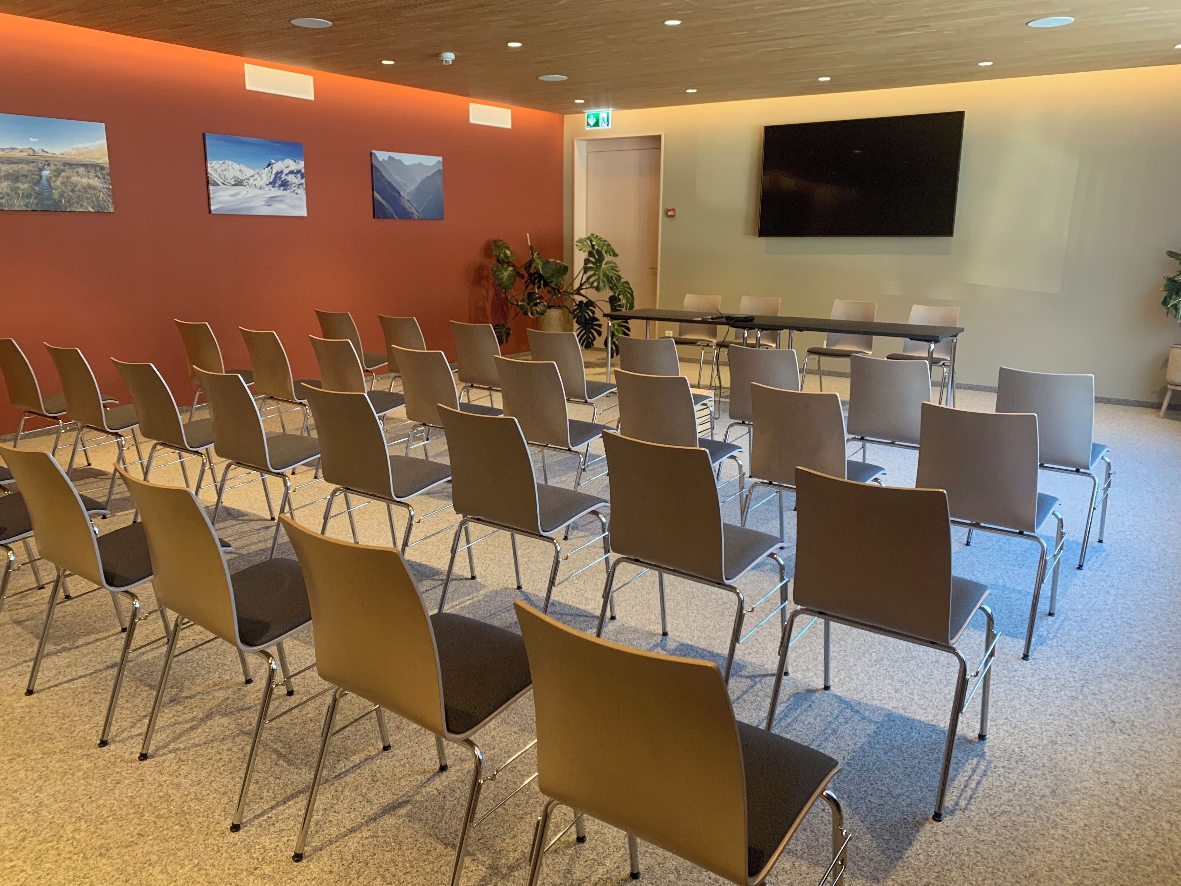 Ein Konferenzraum mit Reihen von Stühlen, einem großen Bildschirm und gerahmten Bildern an der Wand.