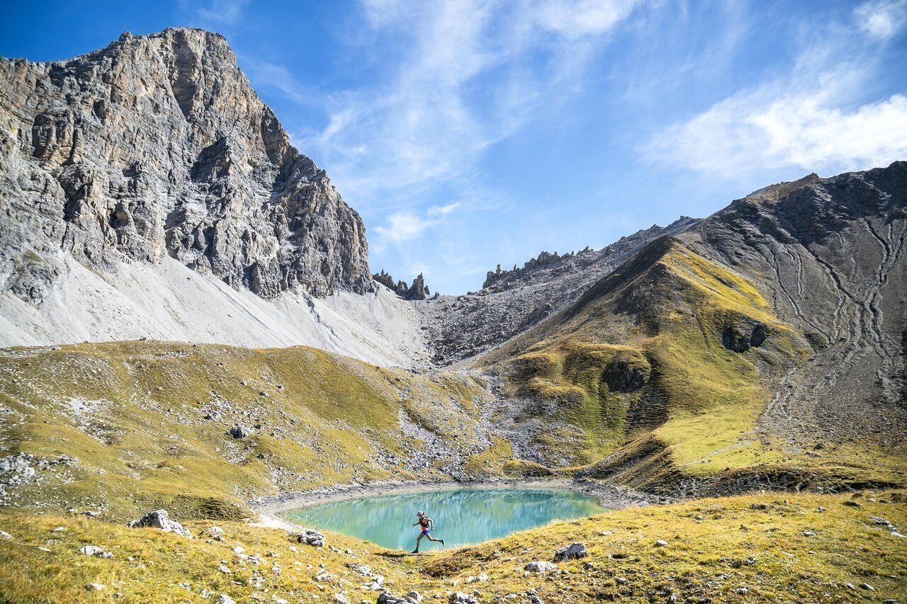 A mountainous landscape with a clear lake and a person running.