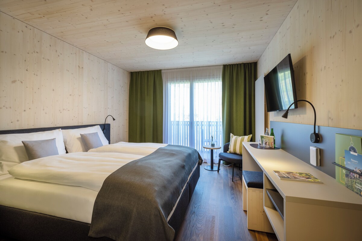 A hotel room with a large bed, a desk with a chair, a TV, and a window with curtains.