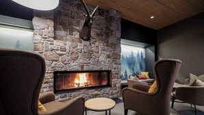 A cozy living room with a stone fireplace, comfortable seating, and a forest mural on the wall. - AVES Hotel Savognin (Surses)