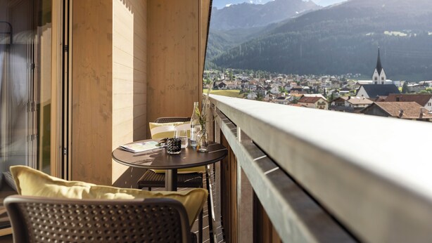 A balcony with a table and chairs, overlooking a town and mountains. - AVES Hotel Savognin (Surses)