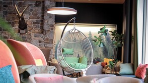 A cozy living room with a stone wall, a hanging chair, and a variety of colorful cushions. - AVES Hotel Savognin (Surses)