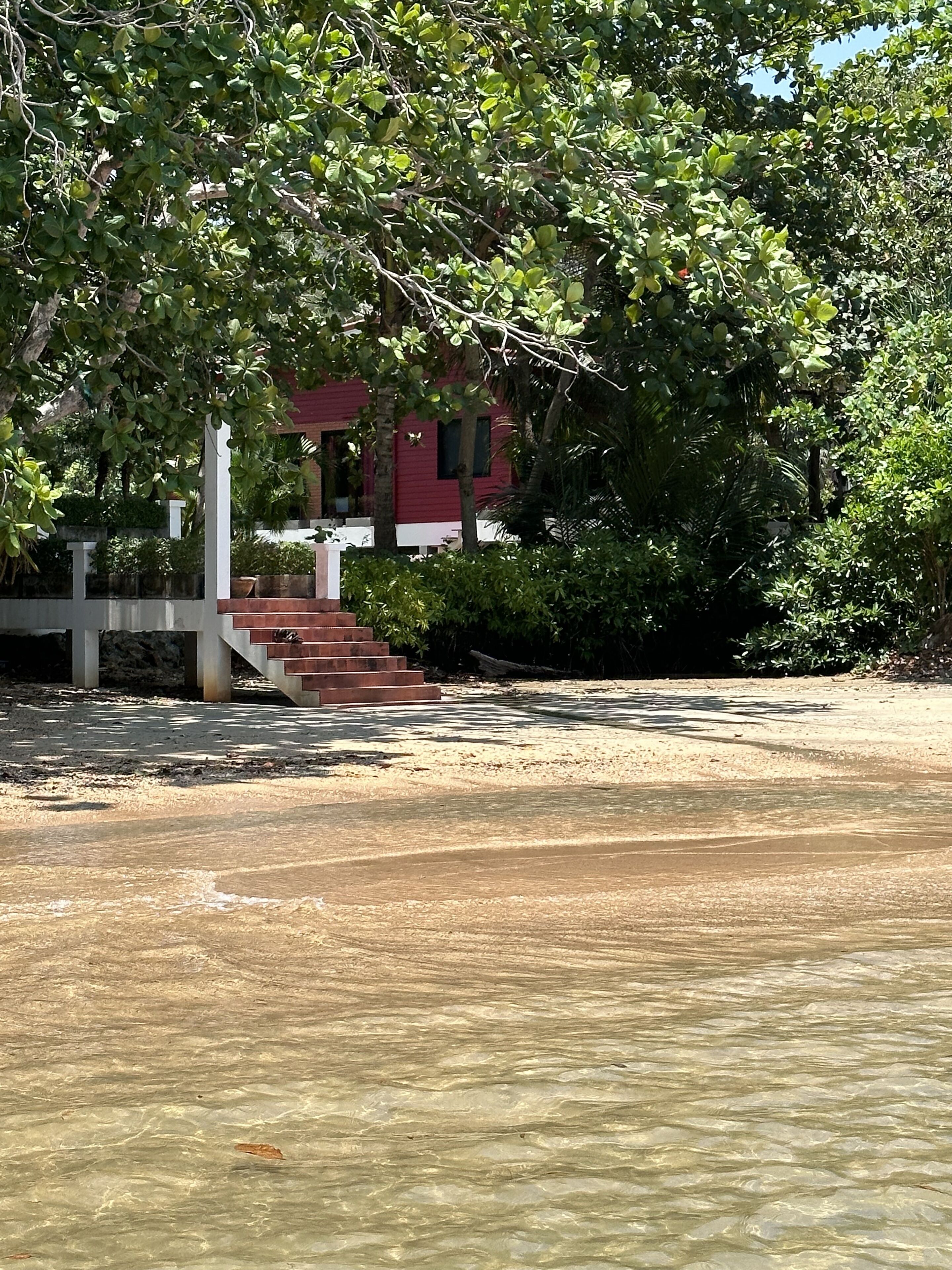 Una playa con agua cristalina, un edificio rojo y una escalera que lleva a una cerca blanca.