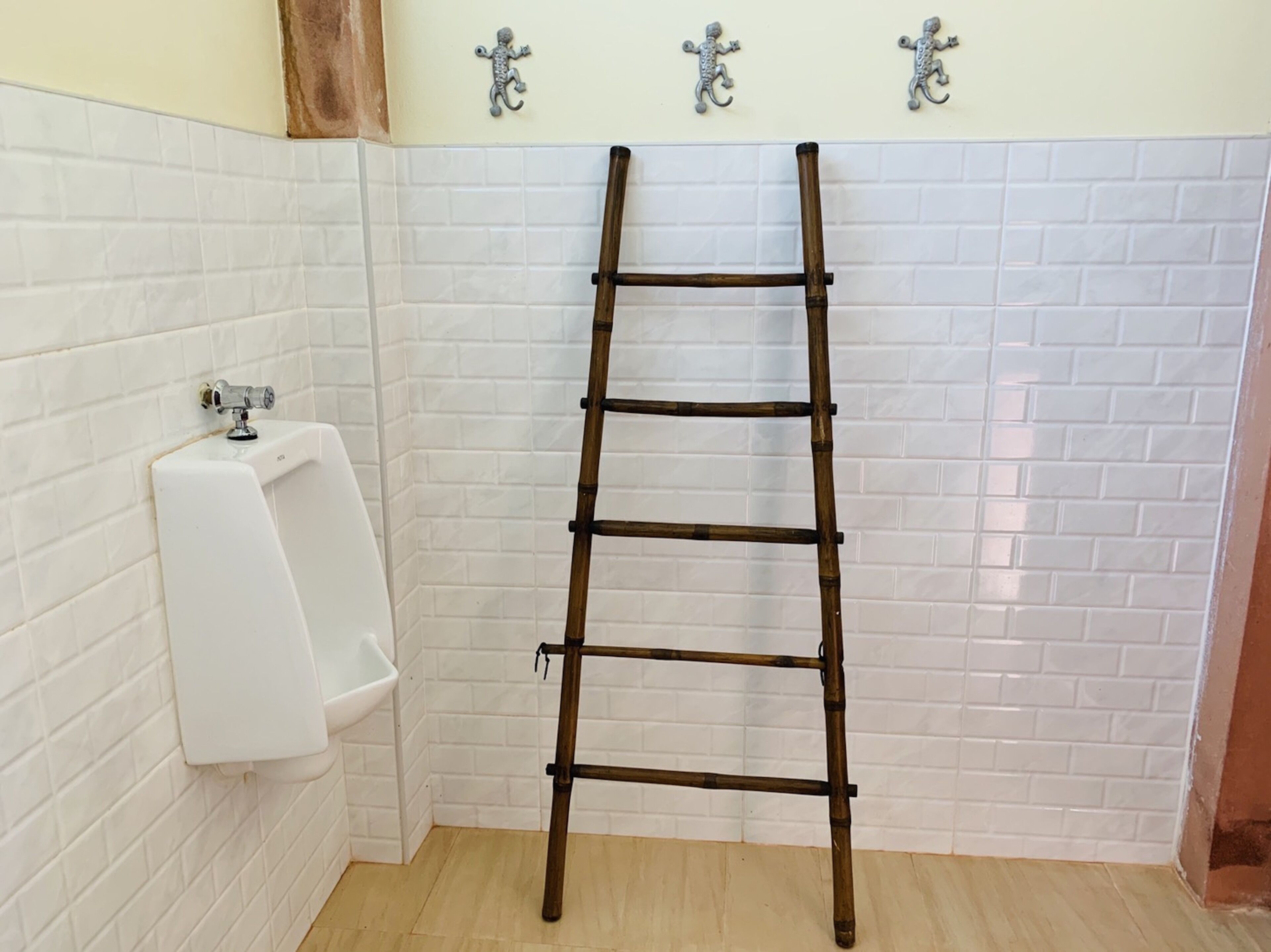 A bathroom with white tiled walls, a white urinal, and a wooden ladder.