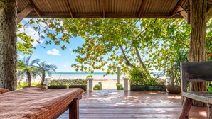 Un molo di legno con una panchina, affacciato su una spiaggia con palme e cielo sereno.