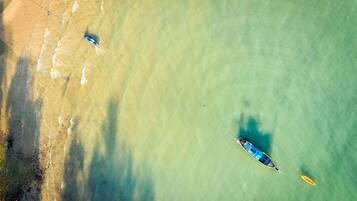 An aerial view of a beach with clear water, a boat, and a surfboard.