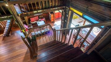Una escalera de madera conduce a un nivel inferior, con vista a una sala de estar acogedora que incluye un sofá y una mesa.