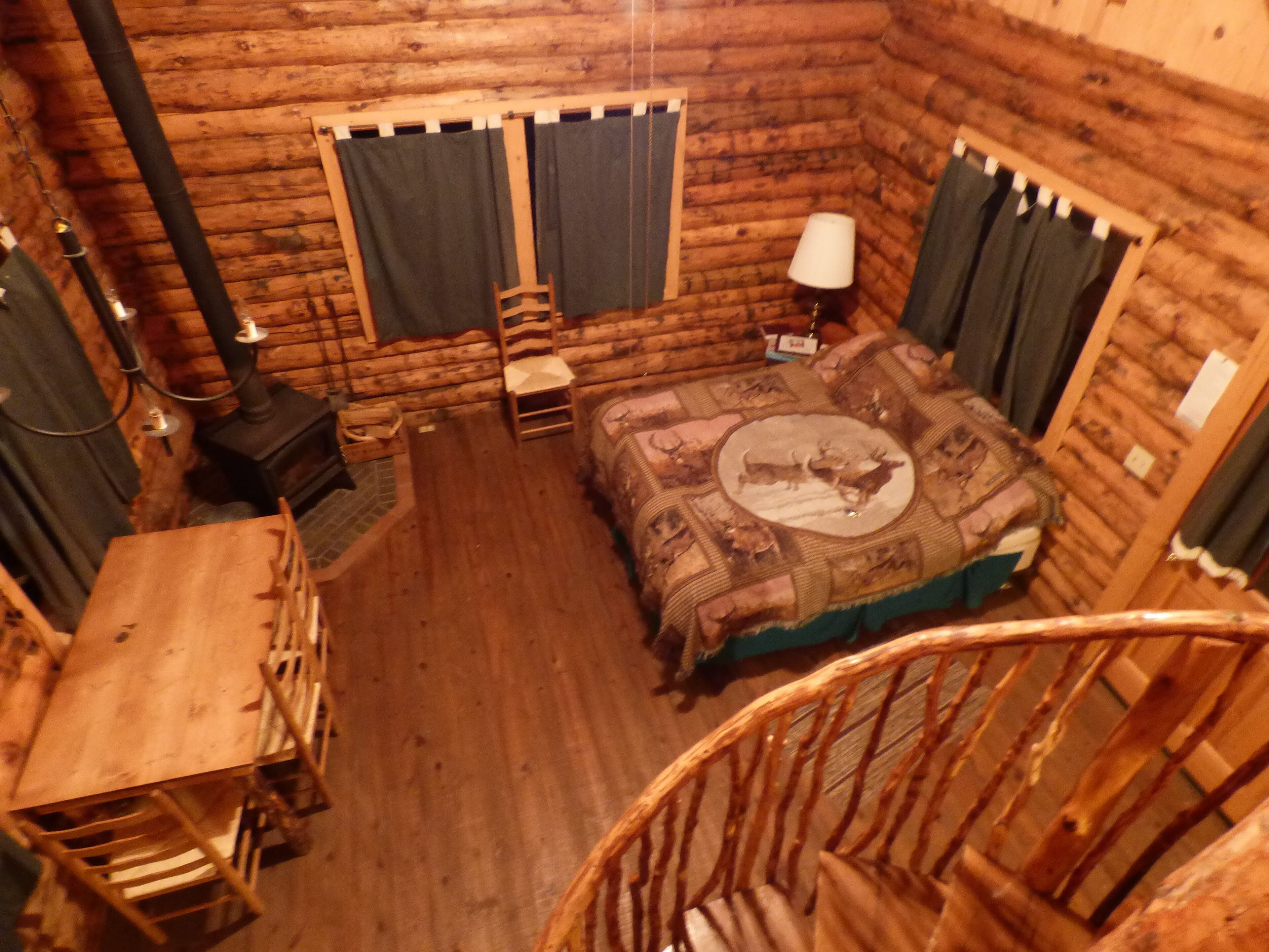 A log cabin bedroom with a bed, a chair, a table, a lamp, and a fireplace.