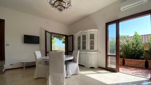 A spacious room with a dining table, chairs, a television, a cabinet, and a large sliding glass door to a patio. - Elegant apartment with view of the sea (Piombino)