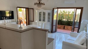 A modern kitchen with a central island, white cabinetry, and a dining area with white chairs. - Elegant apartment with view of the sea (Piombino)