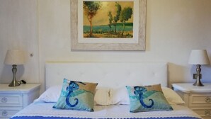 A neatly made bed with a blue bedspread, two decorative pillows, and a framed landscape painting above it. - Elegant apartment with view of the sea (Piombino)