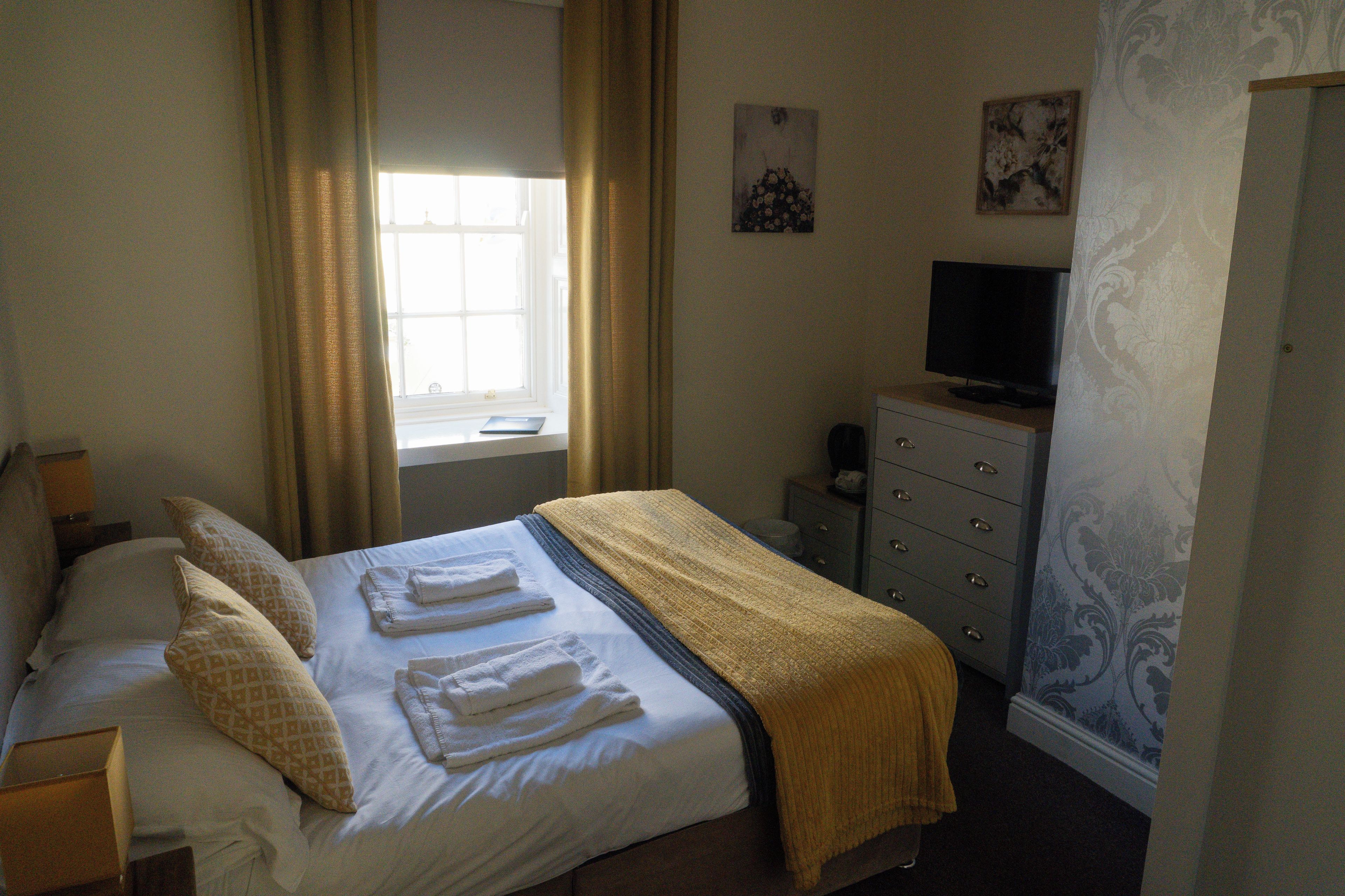 A hotel room with a bed, a television on a dresser, and a window with curtains.
