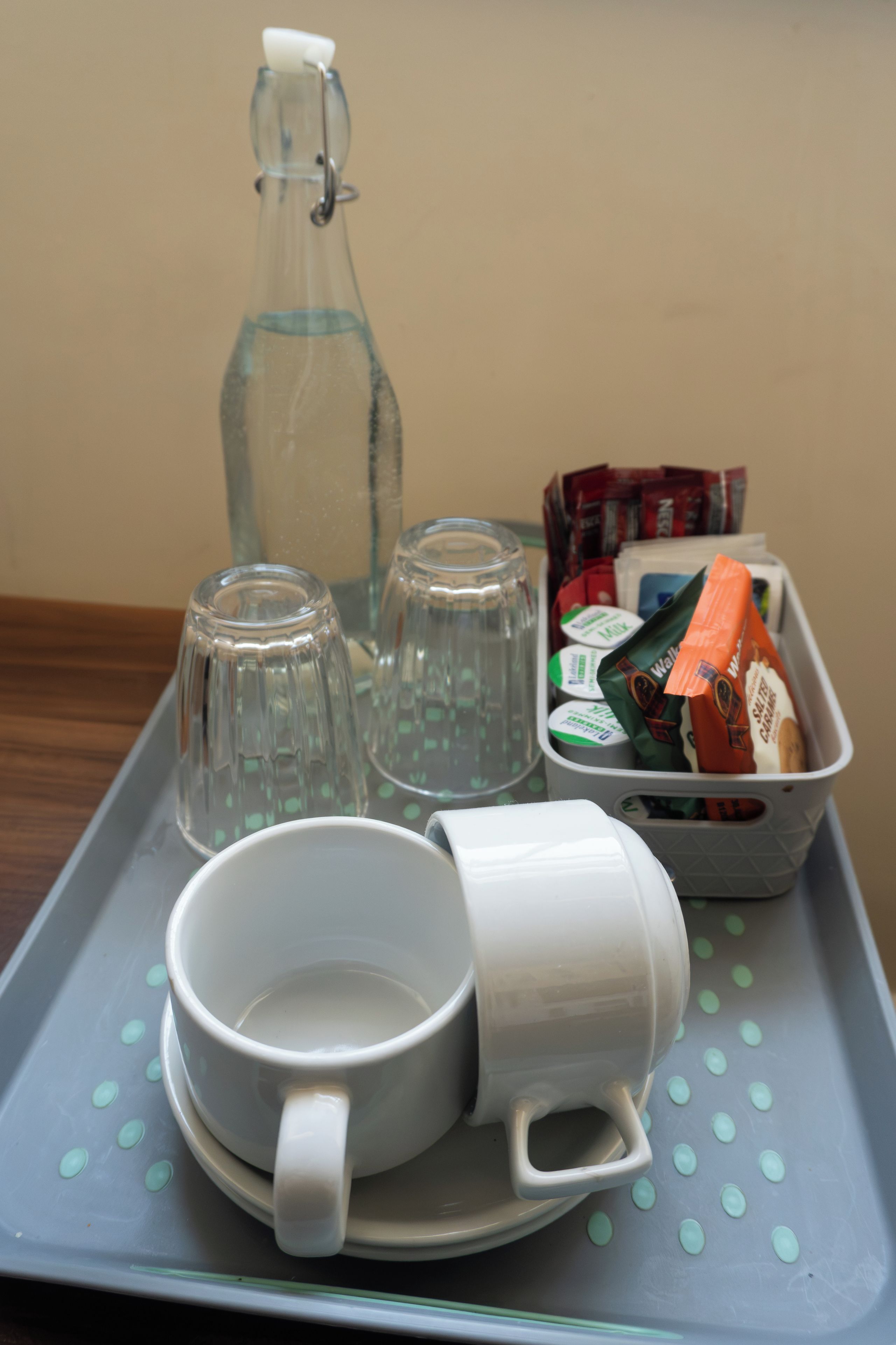 Una bandeja con una botella de vidrio, dos vasos, una taza y un recipiente con aperitivos.