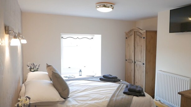 A bedroom with a bed, a wardrobe, a radiator, and a TV mounted on the wall. - Manor House Inn (Haltwhistle)