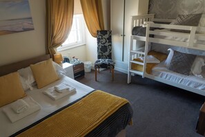 A hotel room with a single bed, a bunk bed, a chair, a desk with a lamp, and a window with curtains. - Manor House Inn (Haltwhistle)